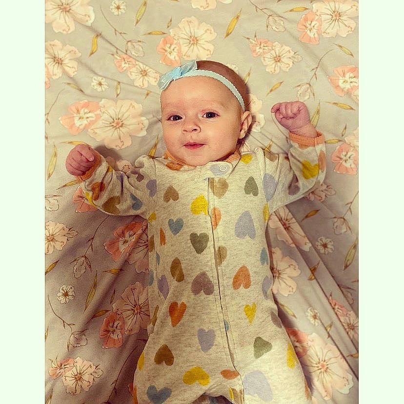 Brynlee is registered to the contest to win money with this photo: baby, baby_products, baby_toddler_clothing, baby_toys, child, dress, face, happy, headwear, linens, magenta, pattern, peach, person, petal, pink, room, sleeve, smile, textile
