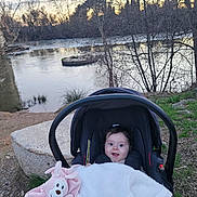 Luna participe au concours pour gagner de l'argent avec cette photo : baby, car_seat, blanket, outdoor, river, trees, grass, rocks, water, nature, child, person, face, happy, smiling, winter, scenery, park, infant, cute