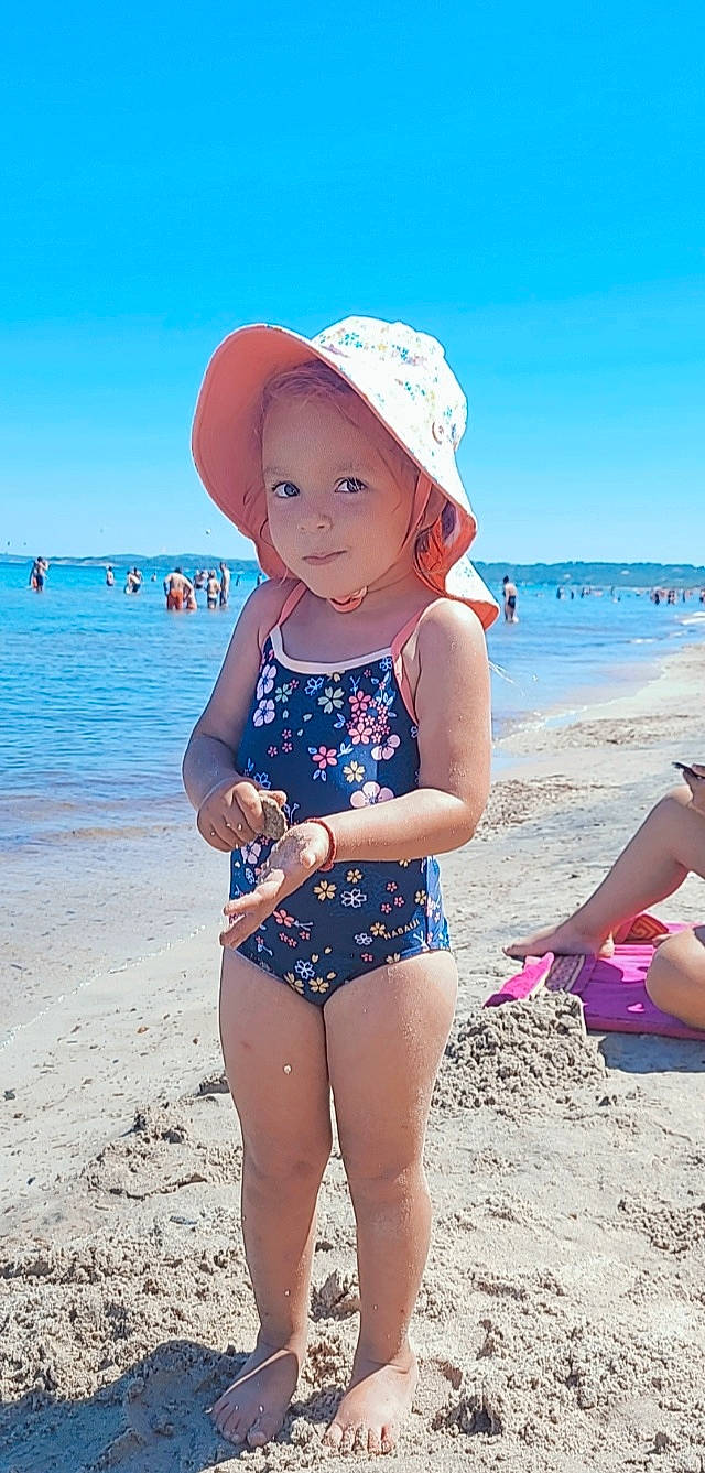 Giulia a rejoint le concours — aidez-le/la à gagner de superbes lots ! beach, blue, clothing, eye, happy, hat, headgear, headwear, leg, leisure, natural_environment, people_on_beach, person, sand, sky, summer, sun_hat, swimwear, thigh, toddler