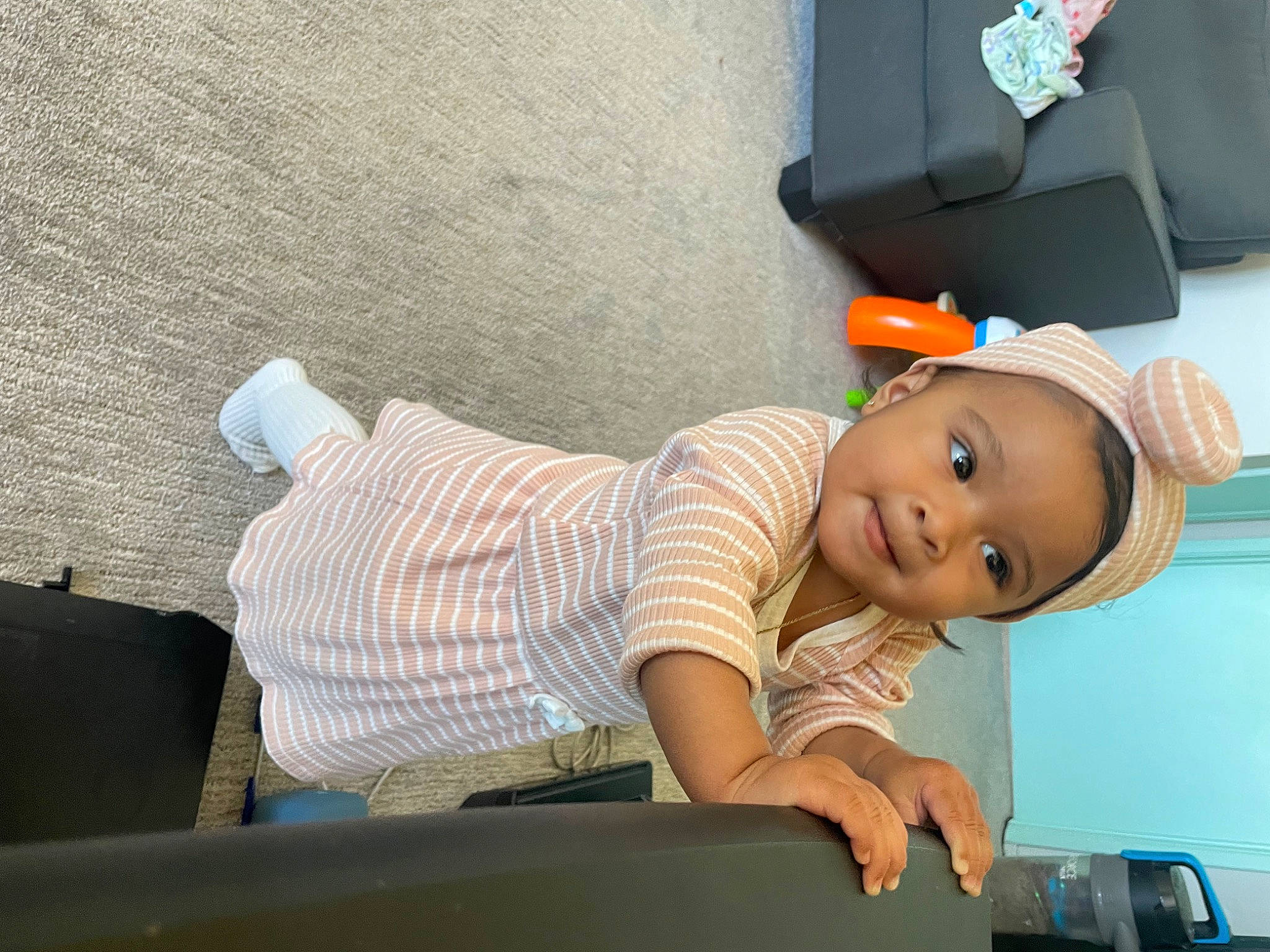 Kailani is registered to the contest to win money with this photo: baby, baby_products, child, comfort, elbow, fashion_accessory, fun, hat, human_leg, knee, person, room, sitting, smile, toddler, vehicle_door