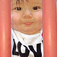 Caspain joined the competition — help win amazing prizes! child, toddler, face, closeup, curious, red_bars, white_shirt, text_on_clothing, outdoor, young_child, smile, eyes, hair, expression, portrait, peeking, playground, bars, innocence, baby
