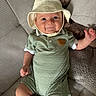 Benny joined the competition — help win amazing prizes! baby, child, hat, romper, green_clothing, plush_toy, teddy_bear, cushion, sofa, smile, face, arm, hand, legs, indoor, comfortable, cute, young, infant, portrait