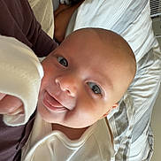 Benny joined the competition — help win amazing prizes! baby, infant, person, sleep_mask, bedroom, blanket, smile, tongue_out, white_clothing, resting, pillow, bed, indoor, holding, happy, cute, face, head, skin, relaxing