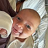 baby, infant, person, sleep_mask, bedroom, blanket, smile, tongue_out, white_clothing, resting, pillow, bed, indoor, holding, happy, cute, face, head, skin, relaxing