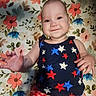 baby, child, smiling, face, hand, tank_top, stars_pattern, shorts, red_checkered, floral_background, blanket, lying_down, cute, happy, infant, person, portrait, indoors, colorful, playful