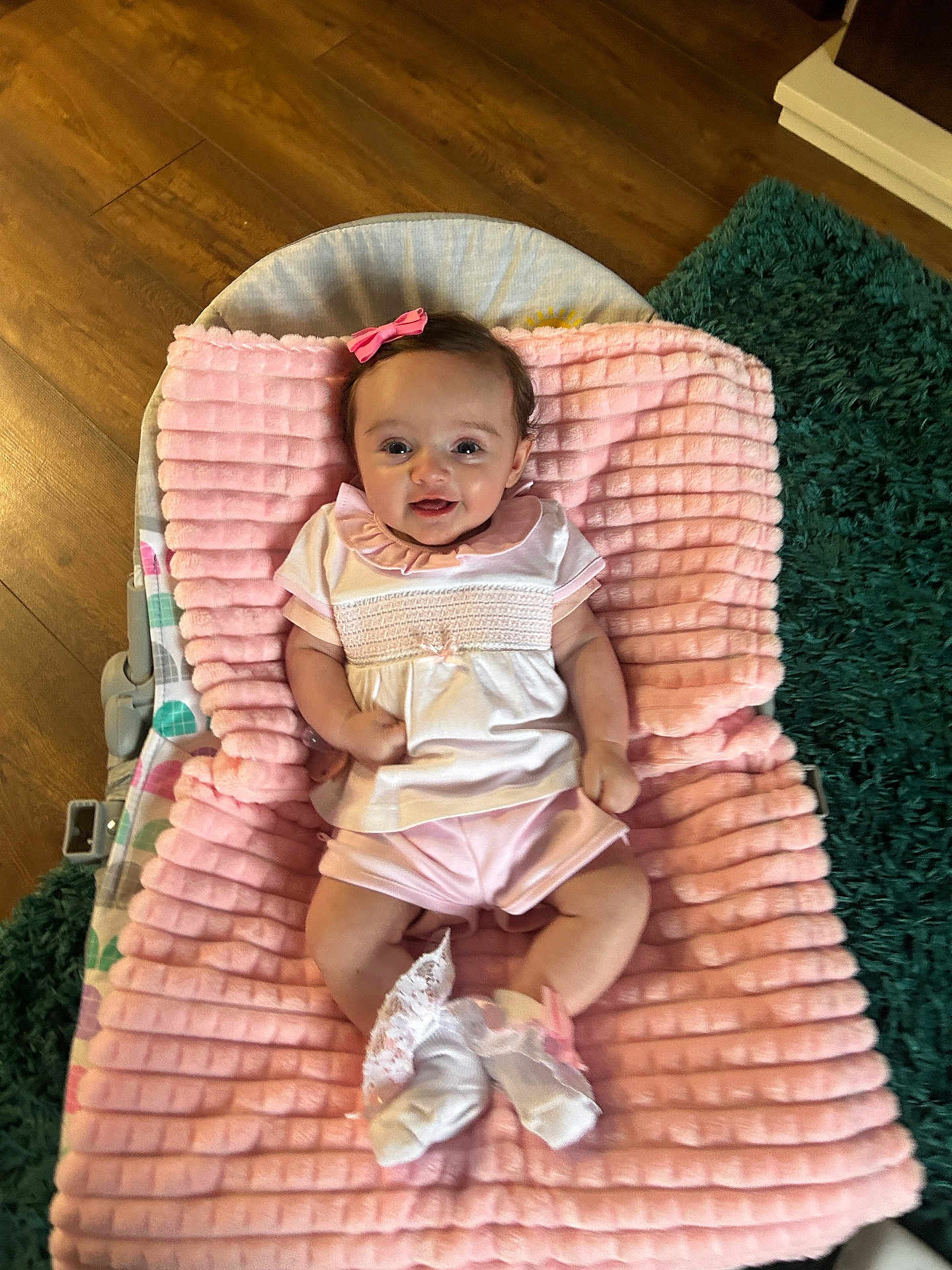 Frankie is registered to the contest to win money with this photo: baby, infant, pink_blanket, smiling, bow, cute, laying_down, socks, lace, pastel_clothing, wooden_floor, green_rug, indoor, child, happy, soft_texture, baby_girl, portrait, comfortable, cozy