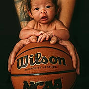 Jersee is registered to the contest to win money with this photo: baby, basketball, closeup, composite_leather, curious, cute, expression, focus, hands, holding, indoor, infant, ncaa, person, portrait, skin, small, sports, tattoo, wilson