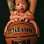 baby, basketball, closeup, composite_leather, curious, cute, expression, focus, hands, holding, indoor, infant, ncaa, person, portrait, skin, small, sports, tattoo, wilson