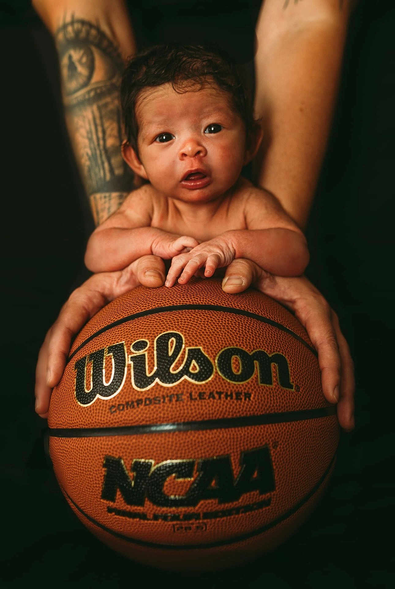 Jersee is registered to the contest to win money with this photo: baby, basketball, closeup, composite_leather, curious, cute, expression, focus, hands, holding, indoor, infant, ncaa, person, portrait, skin, small, sports, tattoo, wilson