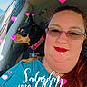 black_dog, car, casual_clothing, daylight, dog, glasses, happy, heart_effect, indoor, long_hair, pet_collar, portrait, red_lipstick, seatbelt, selfie, smile, tan_dog, text_overlay, window, woman