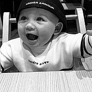 Lou a rejoint le concours — aidez-le/la à gagner de superbes lots ! baby, child, smiling, hat, cap, under_armour, high_chair, table, wood, indoor, black_and_white, happy, cute, clothing, face, person, portrait, expression, joy, toddler