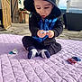 baby, toddler, child, sitting, hoodie, hooded_jacket, toy_cars, pacifier, blanket, purple_blanket, socks, outdoor, patio, paved_floor, surprised_expression, hands, face, playtime, daylight, garden