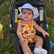 Julia joined the competition — help win amazing prizes! baby, child, car_seat, white_hat, romper, outdoor, tree_trunk, grass, sunlight, smiling, footwear, infant, nature, greenery, cute, summer_clothing, seat, baby_shoes, portrait, happy
