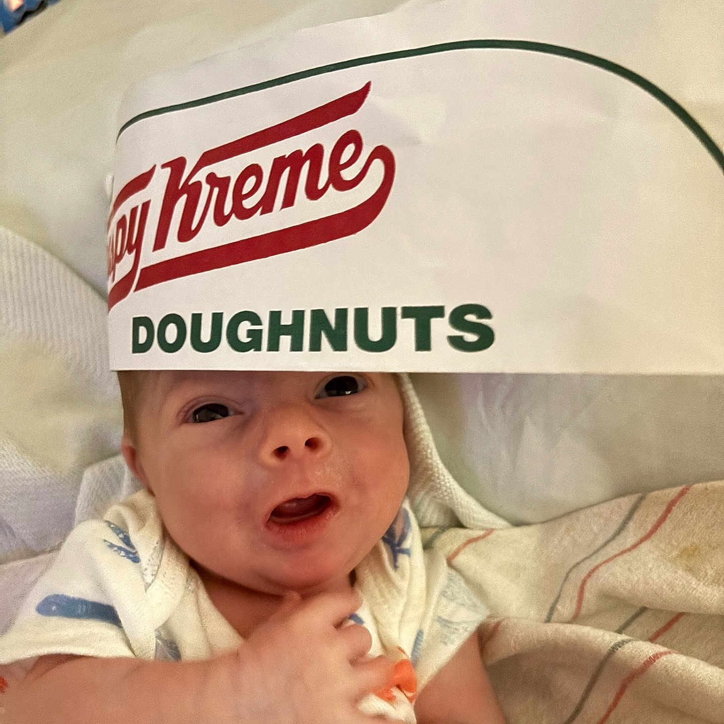 Christian joined the competition — help win amazing prizes! baby, blanket, closeup, clothing, cozy, cute, doughnut_box, expression, fabric, face, food_packaging, hand, headwear, indoors, infant, lying_down, newborn, person, resting, soft
