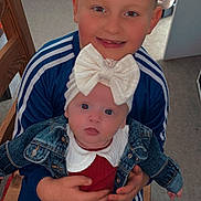 Mya participe au concours pour gagner de l'argent avec cette photo : child, baby, sibling, indoor, portrait, smile, denim_jacket, bow, headwear, blue_clothing, red_clothing, hands, chair, car_seat, floor, person, happy, cute, family, seated