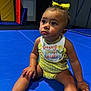 baby, bib, blue_mat, child, clothing, curious, cute, expression, face, floor, hand, indoor, legs, looking_up, play_area, polka_dot, sitting, skin, toddler, yellow_bow