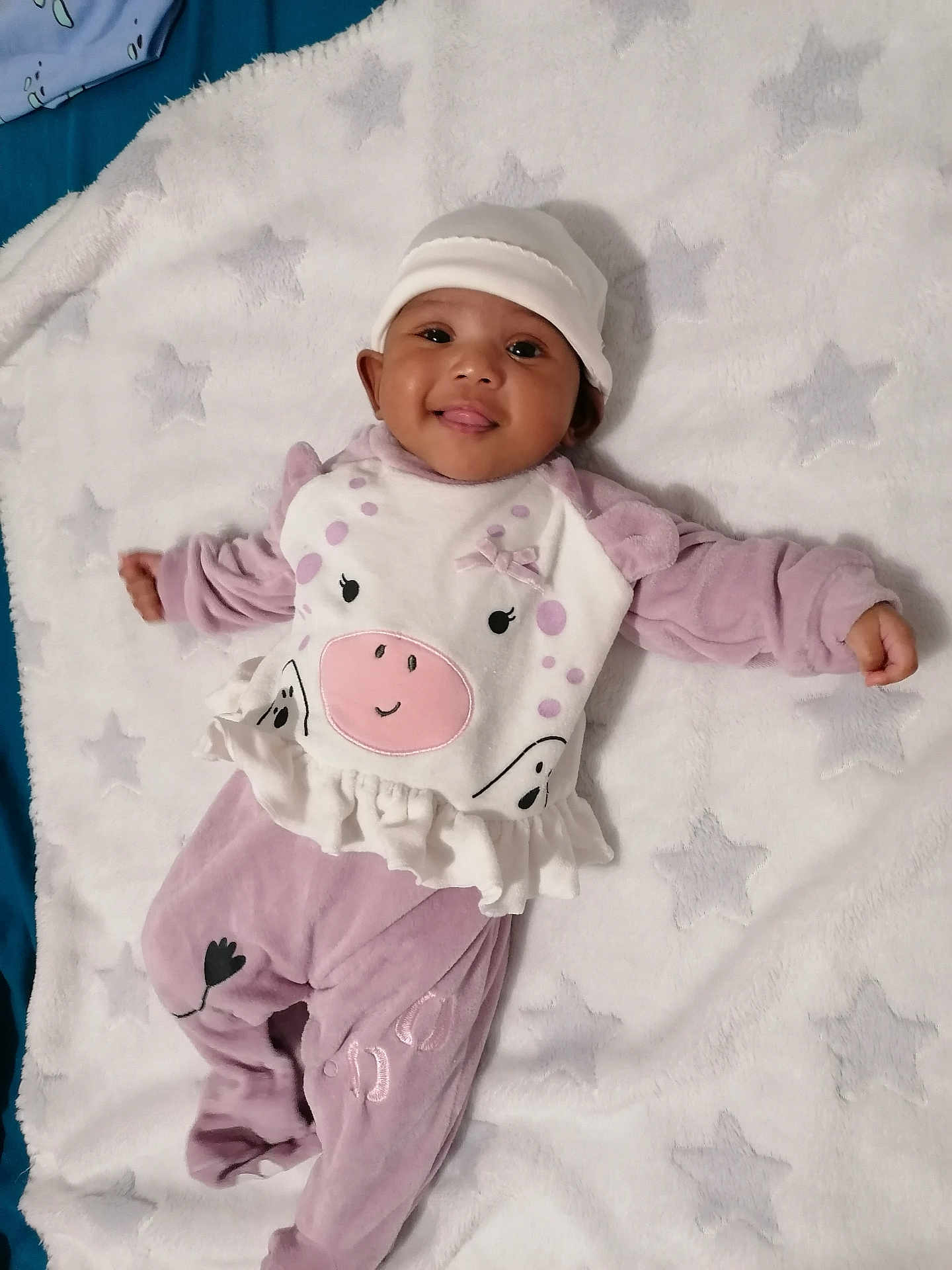 Kailea a rejoint le concours — aidez-le/la à gagner de superbes lots ! baby, infant, smiling, tongue_out, hat, purple_clothing, white_clothing, blanket, star_pattern, lying_down, cute, soft_texture, face, child, indoors, happy, one_person, portrait, playful, cozy
