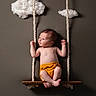 baby, infant, swing, rope, wooden_swing, clouds, cotton_clouds, indoor, nursery, child, cute, portrait, yellow_shorts, bare_chest, soft_lighting, background, curious, small_feet, newborn, studio_photo