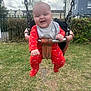 baby, swing, playground, outdoor, grass, fence, smiling, child, red_clothing, onesie, chain, park, happy, face, person, daytime, building, sky, fun, joy