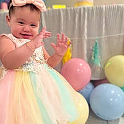 Emma is registered to the contest to win money with this photo: baby, child, tutu_dress, bow_headband, smiling, happy, balloons, pastel_colors, celebration, party, curtain, floor_tiles, jewelry, bracelet, person, portrait, indoor, cute, hands, toddler