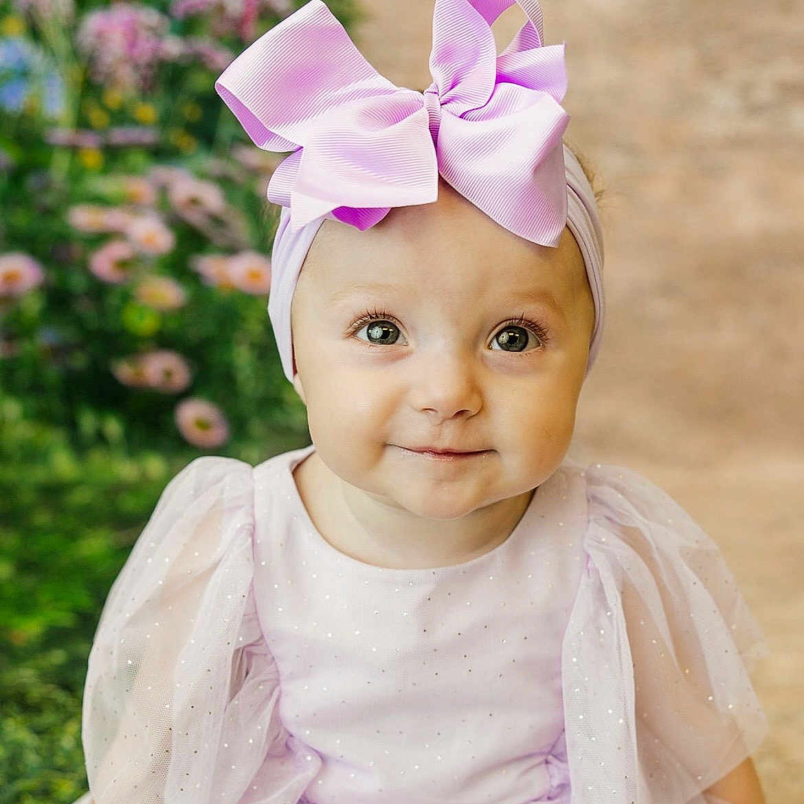 Imara joined the competition — help win amazing prizes! apparel, baby, bow, child, cute, dress, eyes, face, flowers, garden, girl, headband, lavender, outdoor, pink, portrait, sitting, smiling, toddler, young