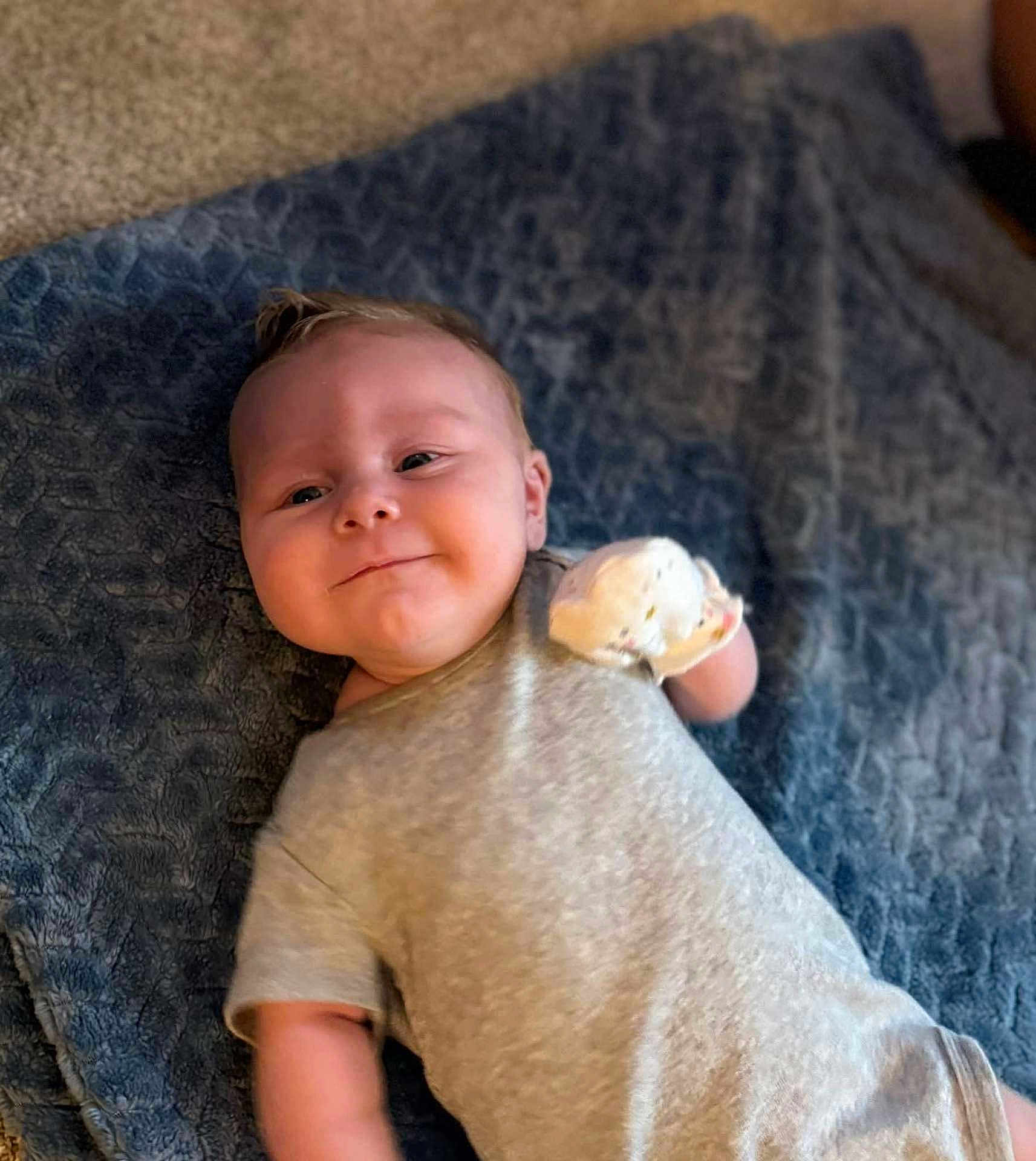 Samuel joined the competition — help win amazing prizes! baby, infant, smiling, blanket, blue_blanket, onesie, mitten, lying_down, indoor, child, cute, happy, face, skin, young, person, portrait, soft_texture, carpet, cozy
