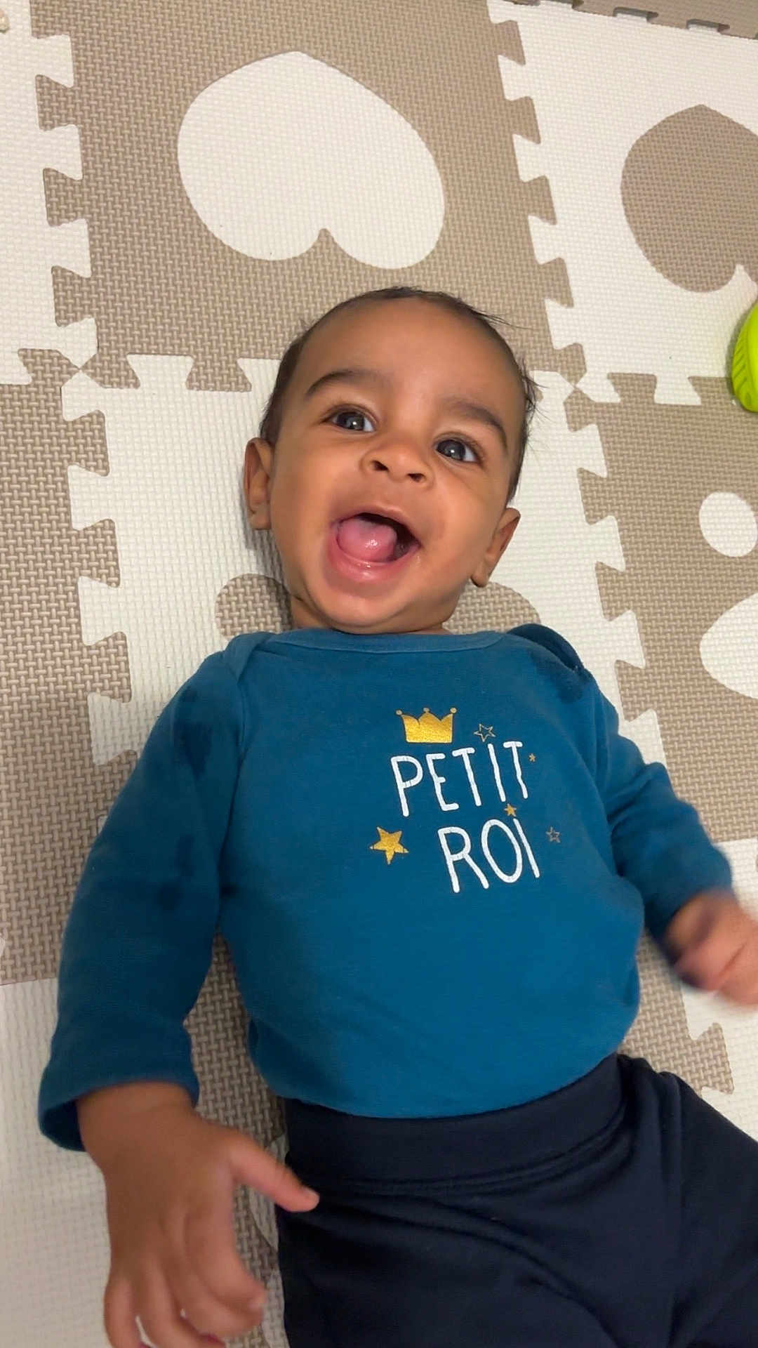 Cameron a rejoint le concours — aidez-le/la à gagner de superbes lots ! baby, child, smiling, blue_shirt, text_on_clothing, play_mat, indoor, happy, person, infant, cute, lying_down, patterned_mat, long_sleeves, dark_pants, small_hand, closeup, cheerful, young_child, portrait