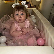 Tilly-May joined the competition — help win amazing prizes! baby, child, pink_dress, bows, plastic_balls, play_area, padded, indoor, curious, cute, chubby_cheeks, seated, soft_lighting, playpen, tulle, infant, portrait, person, toddler, hands_clasped
