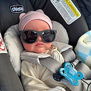 Lydia is registered to the contest to win money with this photo: baby, car_seat, sunglasses, pink_hat, pacifier, infant, child, seatbelt, clothing, cute, baby_girl, hat, gray_harness, indoor, portrait, baby_accessory, baby_clothes, car_interior, baby_face, relaxing