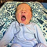 baby, infant, yawning, pajamas, blanket, patterned_blanket, indoor, furniture, television, couch, face, person, newborn, sleepy, cute, child, home, relaxing, cozy, soft_lighting