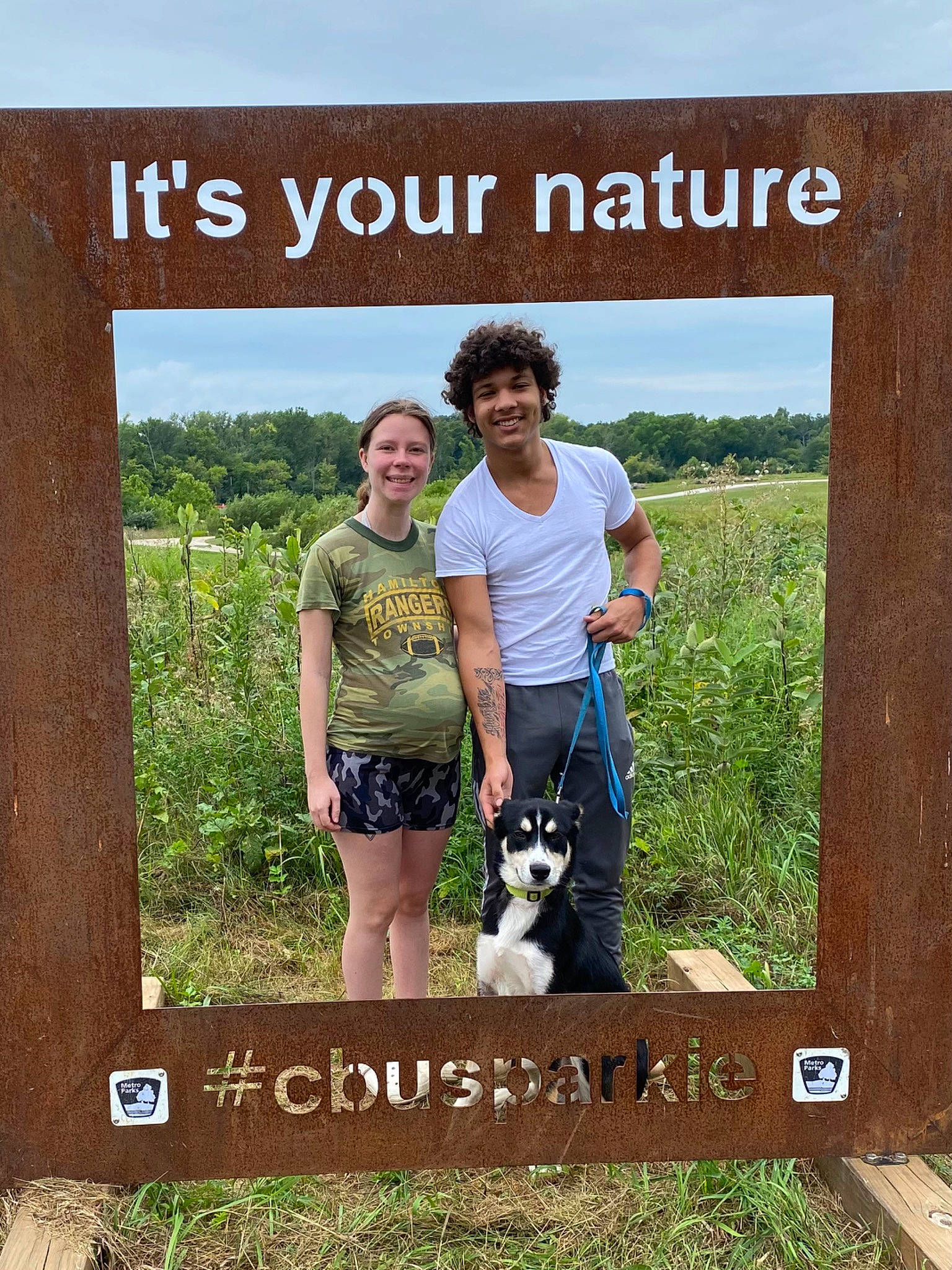 Dave is registered to the contest to win money with this photo: adaptation, biome, carnivore, dog, ecoregion, fawn, grass, happy, landscape, mammal, natural_environment, natural_landscape, nature, people_in_nature, plant, plant_community, shorts, sky, smile, t_shirt