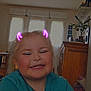 blonde_hair, blue_shirt, cabinet, child, crossed_arms, curtains, devil_horns_filter, earrings, furniture, girl, happy, home, indoor, plant, playful, portrait, smiling, toy, window, yellow_earrings