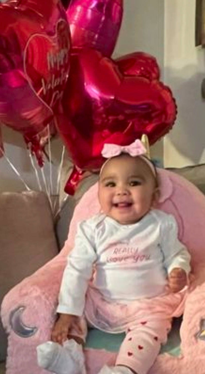 Auria H is registered to the contest to win money with this photo: baby, baby_toddler_clothing, cheek, child, comfort, event, face, fun, happy, headwear, joy, magenta, person, petal, photograph, pink, product, sitting, skin, sleeve