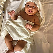 Muhammad is registered to the contest to win money with this photo: baby, towel, bed, white, blanket, child, cute, smiling, tongue_out, infant, soft, sleepwear, happy, playful, skin, lying_down, indoors, hooded_towel, person, newborn