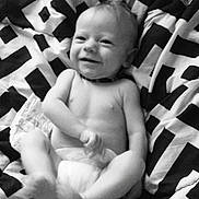 Atlys is registered to the contest to win money with this photo: baby, infant, child, smiling, lying_down, diaper, blanket, black_and_white, portrait, face, happy, indoor, bedding, patterned_blanket, photograph, phone_screenshot, screen, relaxed, cute, eyes