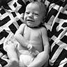 baby, infant, child, smiling, lying_down, diaper, blanket, black_and_white, portrait, face, happy, indoor, bedding, patterned_blanket, photograph, phone_screenshot, screen, relaxed, cute, eyes