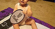 Kailee joined the competition — help win amazing prizes! toddler, child, baby, sitting, barefoot, smiling, portrait, indoors, quilt, blanket, purple, wooden_furniture, carpet, room, toy, prop, round_sign, happy, face, photography