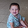 baby, blue_clothing, child, diaper_wipes, dress, face, floor, happy, household_item, indoor, infant, laughing, lifestyle, packaging, playful, portrait, short_hair, sitting, smiling, tile