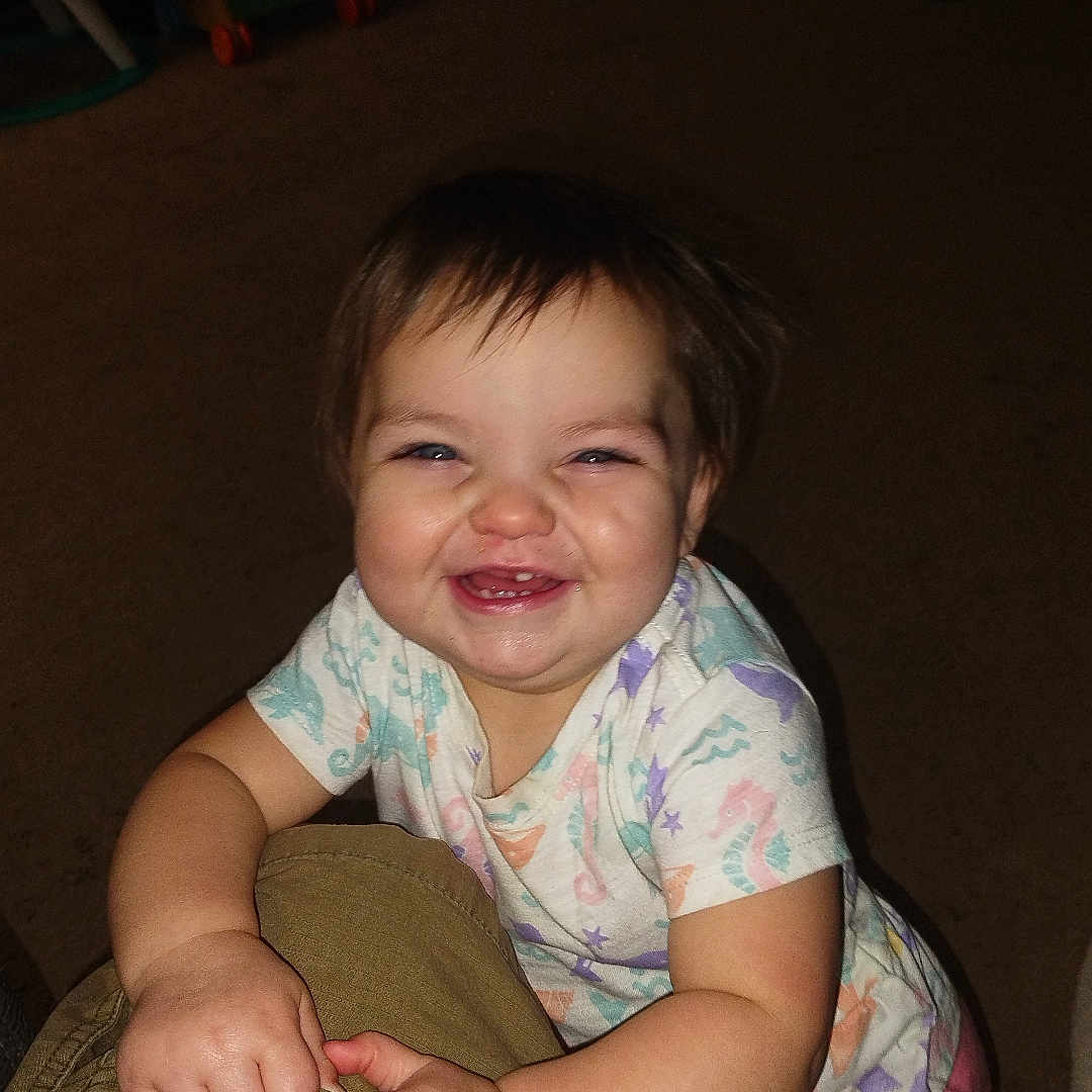 Kailee joined the competition — help win amazing prizes! baby, child, toddler, smiling, happy, laughing, portrait, face, indoors, home, carpet, toys, playroom, clothing, shirt, pink_pants, sitting, crawling, adult_leg, flash_photography