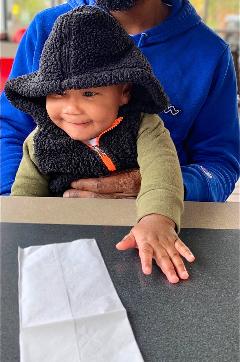 Hezekiah is registered to the contest to win money with this photo: baby, blue, cap, child, electric_blue, fun, grass, happy, hat, headwear, jacket, joy, knit_cap, leisure, outerwear, person, photograph, recreation, sitting, smile