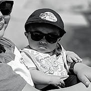 Kenai is registered to the contest to win money with this photo: baby, child, sunglasses, cap, person, arm, hand, clothing, outdoor, portrait, black_and_white, cool, fashion, cute, infant, hat, holding, sunlight, casual, baby_bib