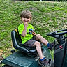 Jasper joined the competition — help win amazing prizes! child, boy, smiling, green_shirt, shorts, sneakers, riding_mower, seat, outdoor, grass, nature, sunny_day, happy, playful, snack, hair, fence, metal_rail, steering_wheel, casual