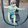 child, toddler, playground, exercise_equipment, outdoor, grass, sandals, shorts, tshirt, seat, arms_outstretched, play, summer_clothing, curly_hair, young_child, recreation, park, leisure, fun, shoes
