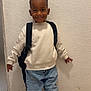 Nahïl a rejoint le concours — aidez-le/la à gagner de superbes lots ! child, boy, smiling, white_sweatshirt, blue_jeans, sneakers, backpack, standing, indoor, wall, floor, casual_clothing, happy, portrait, fashion, young, person, feet, hands, head