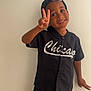 child, boy, peace_sign, smile, black_clothing, cap, shorts, shirt, standing, indoor, wall, happy, gesture, casual, portrait, person, fashion, youth, cute, posing