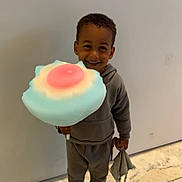 Nahïl a rejoint le concours — aidez-le/la à gagner de superbes lots ! child, smiling, cotton_candy, toy, blanket, indoor, floor, marble, wall, slippers, clothing, hoodie, pants, happy, person, cute, fun, colorful, standing, young