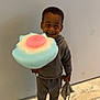 child, smiling, cotton_candy, toy, blanket, indoor, floor, marble, wall, slippers, clothing, hoodie, pants, happy, person, cute, fun, colorful, standing, young