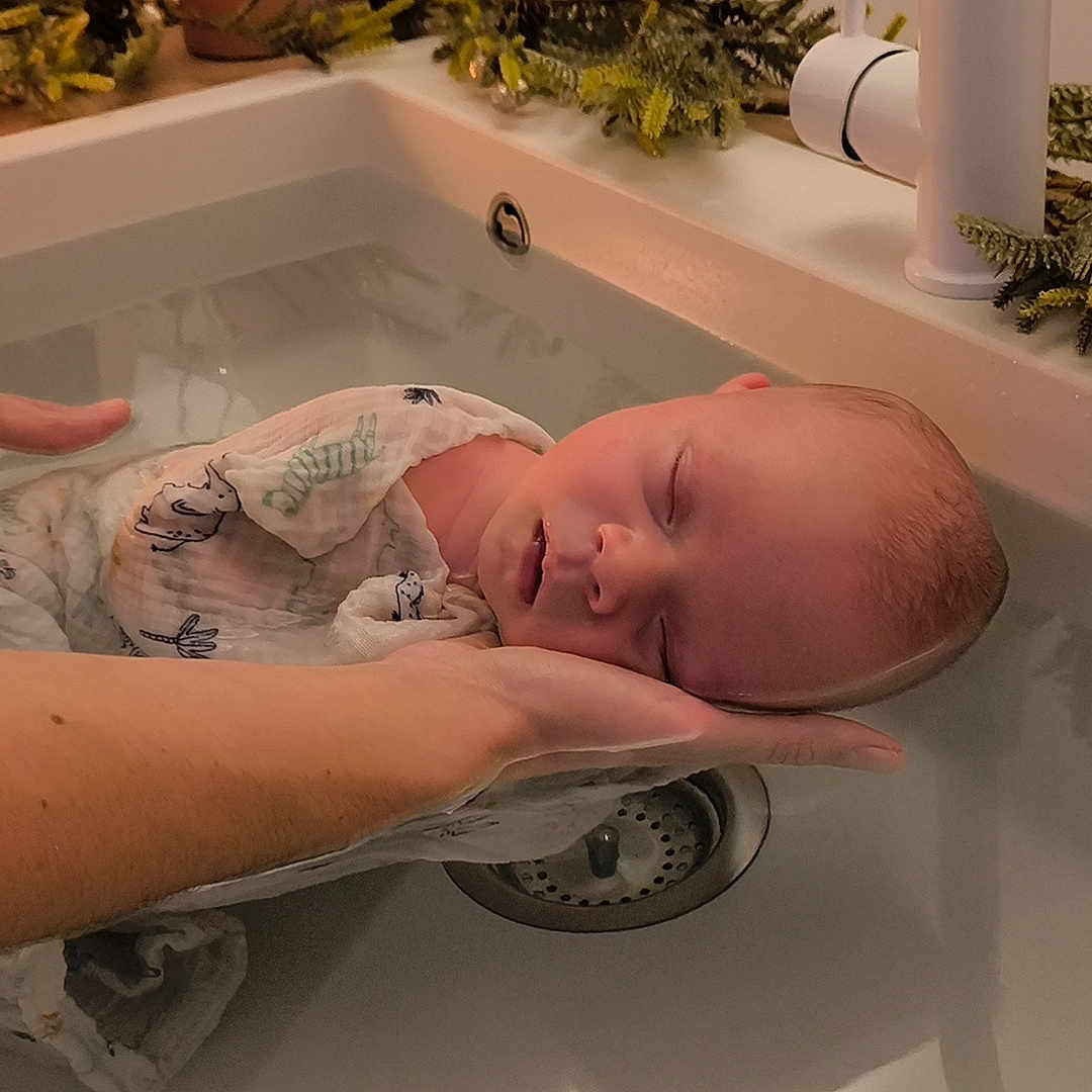 Louis a rejoint le concours — aidez-le/la à gagner de superbes lots ! baby, bath, cloth, drain, faucet, greenery, hands, holiday_decor, indoor, infant, newborn, pinecones, relaxation, serene, sink, sleeping, soft_lighting, tender, water, wrapped