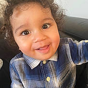 Gebril a rejoint le concours — aidez-le/la à gagner de superbes lots ! child, toddler, smiling, curly_hair, big_eyes, plaid_shirt, button_up_shirt, blue_shirt, portrait, close_up, cute, happy, indoors, couch, face, cheeks, infant, person, playful, warm_lighting