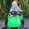 baby, blue_eyes, child, corn_field, dirt, grass, green, happy, nature, outdoor, person, plaid_shirt, plants, play, portrait, seatbelt, smiling, toy_tractor, vehicle, wheels